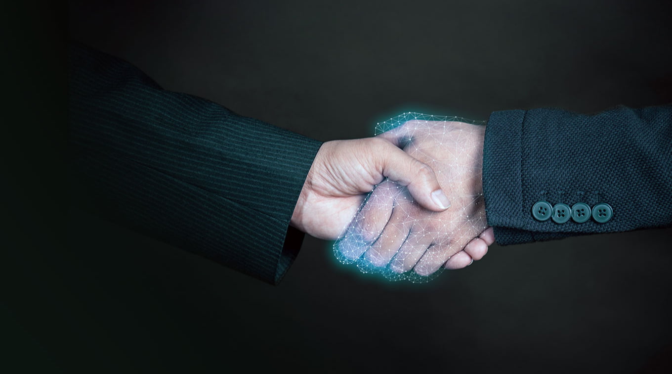 Close-up of two hands shaking, one in a black suit and the other in a grey suit. The handshake is partially represented with a glowing, digital effect, symbolizing partnership and collaboration in a modern context.